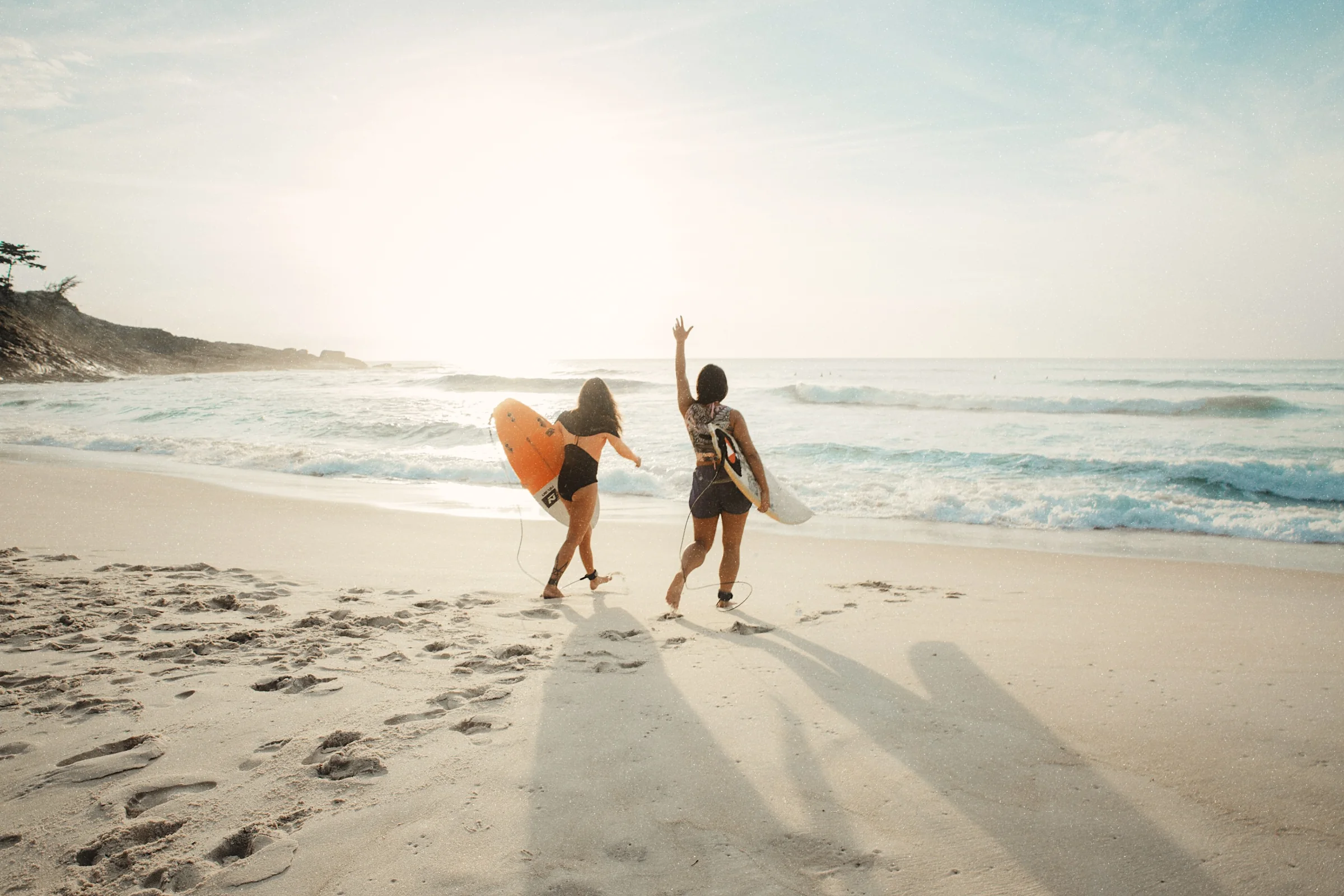 Two surfers walking along a beach towards the low sun, developed in the Heritage look